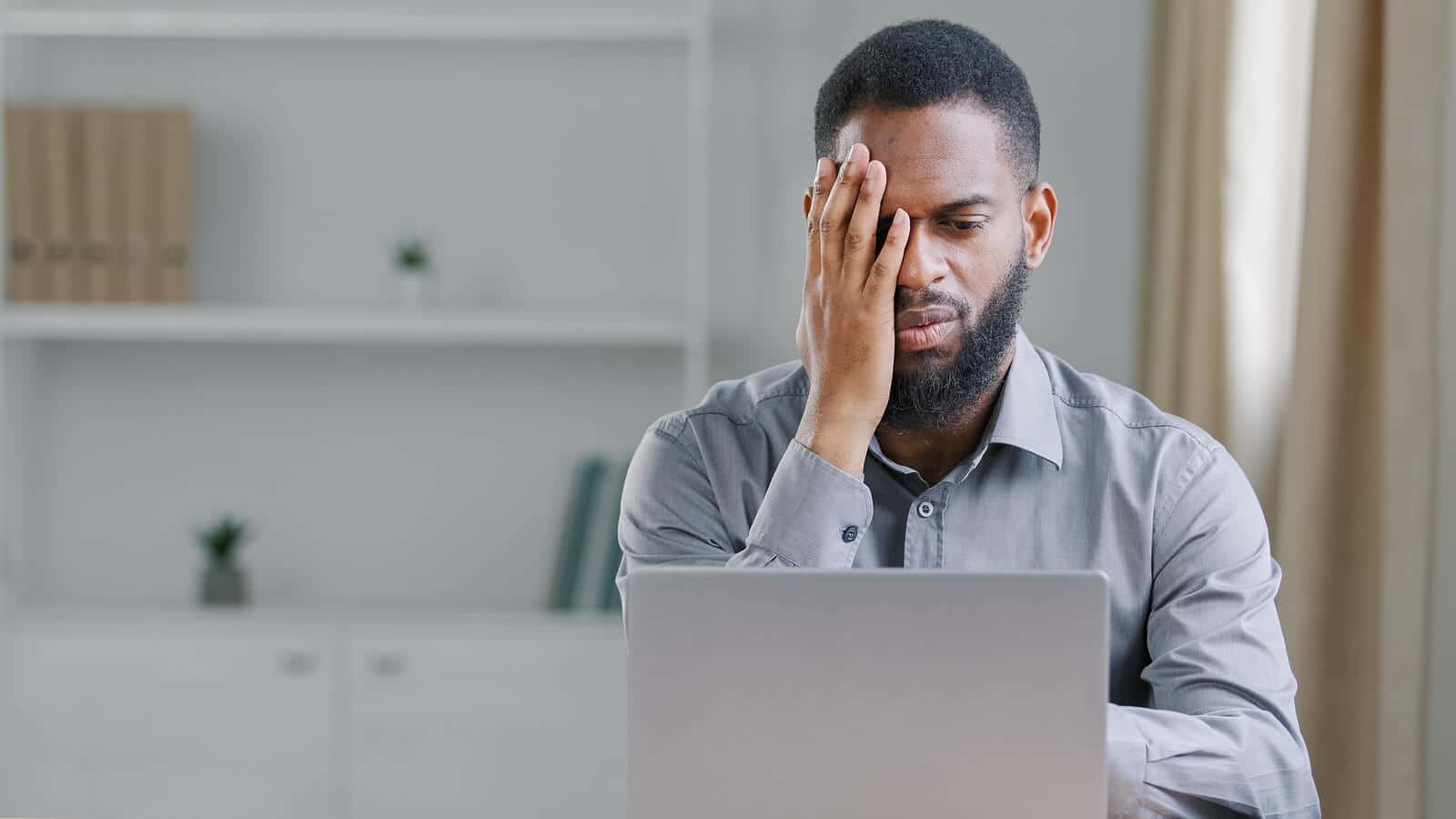 man in front of computer with palm against his head.