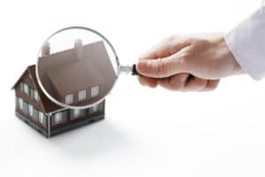 A hand holds a magnifying glass over a miniature house.